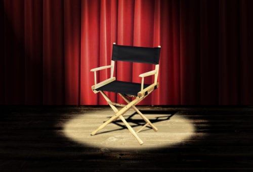 A directors chair on a stage with a red curtain and spotlight