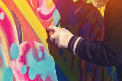 Grafitti artist spraying brightly colored designs on a wall
